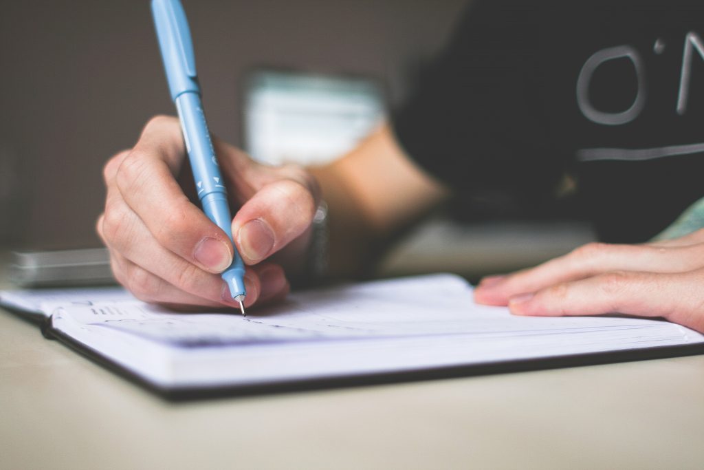 Person holding blue ballpoint pen writing in notebook