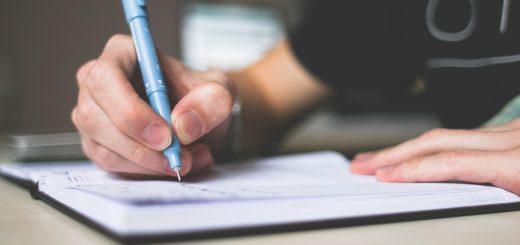Person holding blue ballpoint pen writing in notebook