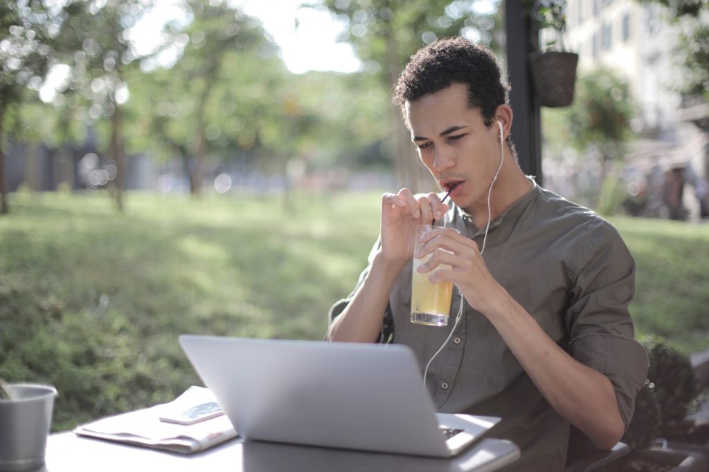 Black man drinking lemonade in cafe and using laptop